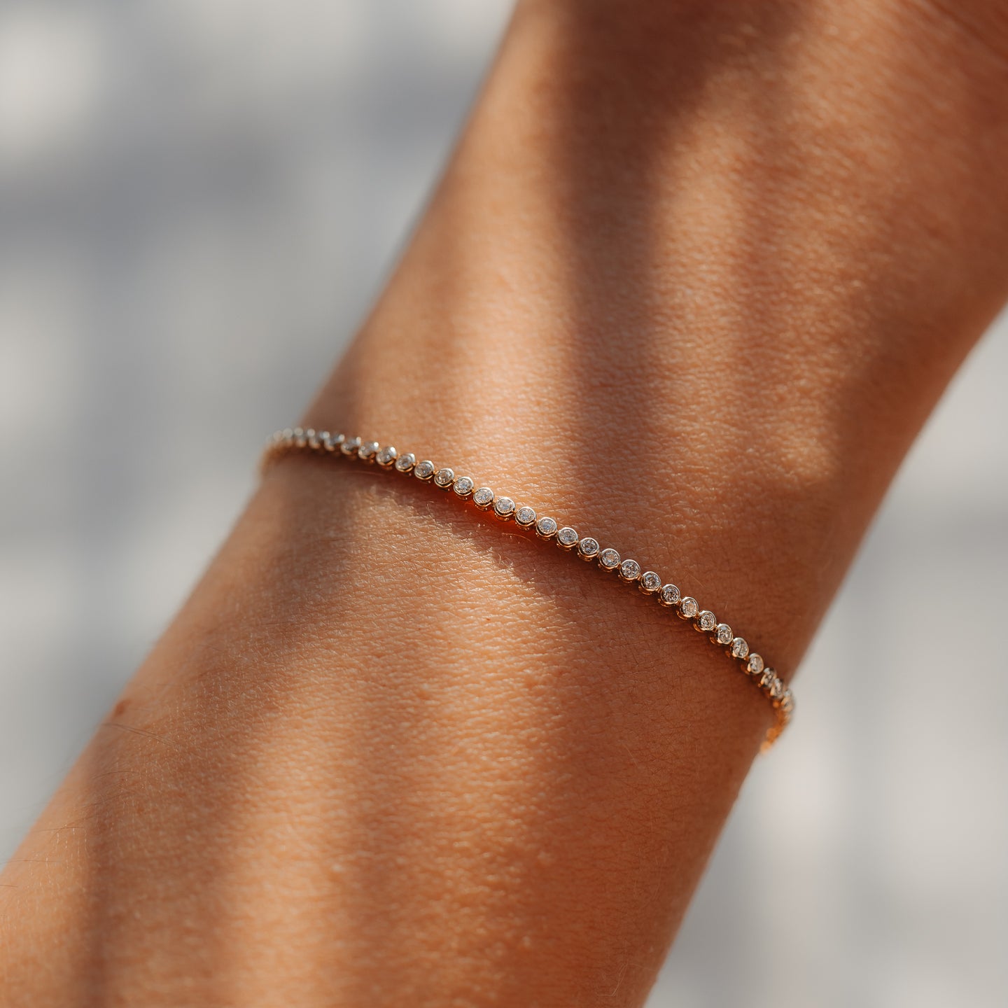 Primo piano di un delicato bracciale tennis in oro giallo 14K con piccoli diamanti rotondi indossato al polso, illuminato da una morbida luce naturale.