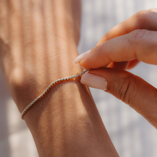 Primo piano di una mano che chiude un bracciale tennis in oro giallo 14K con diamanti al polso alla calda luce del sole.