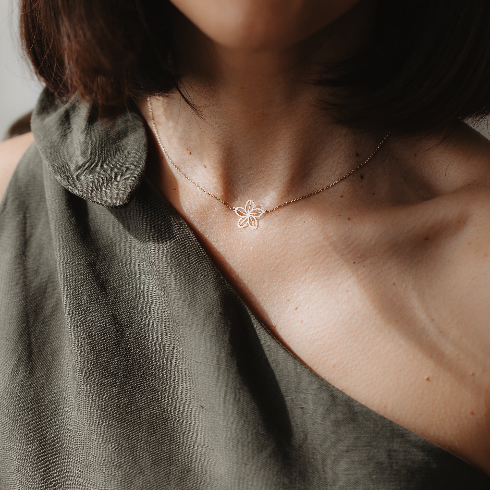 Primo piano di una modella che indossa la collana Wildflower in oro giallo 14K con pendente a delicato profilo di fiore, mostrata all'altezza della clavicola in luce naturale.