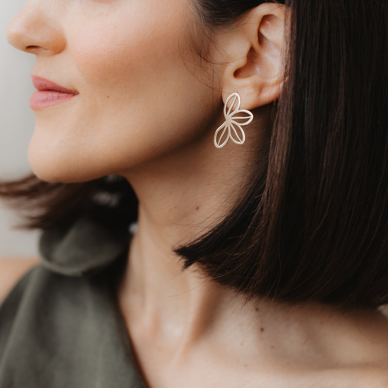 Primo piano di una modella che indossa l'orecchino a lobo Half Wildflower in oro giallo 14K con design a petali aperti; luce morbida in interni e sfondo neutro.