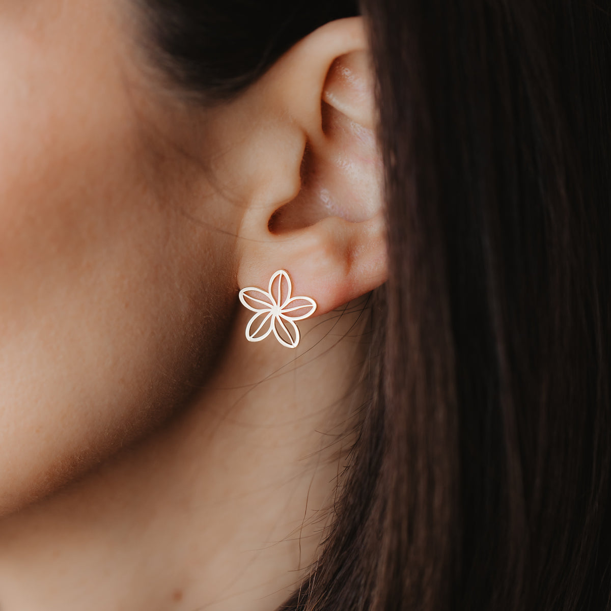 Primo piano di un orecchio con un delicato orecchino a perno a fiore traforato in oro giallo 14K.