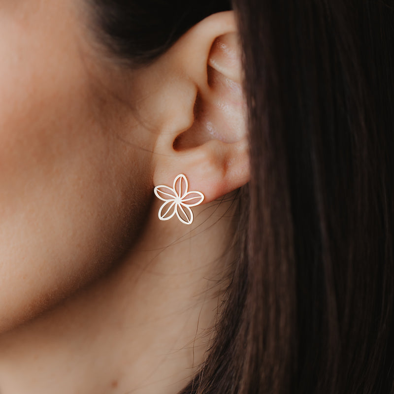 Primo piano di un orecchio con un delicato orecchino a perno a fiore traforato in oro giallo 14K.