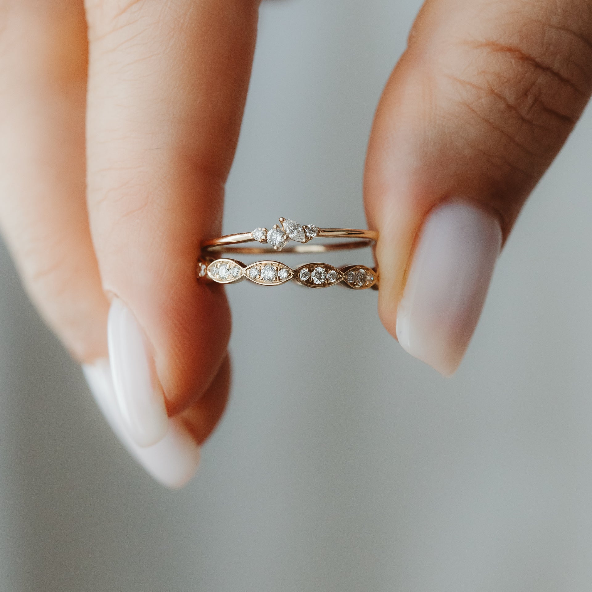 Primo piano di due anelli impilabili in oro giallo 14K con diamanti, tenuti tra le dita — uno con un piccolo cluster e uno con elementi a forma marquise.