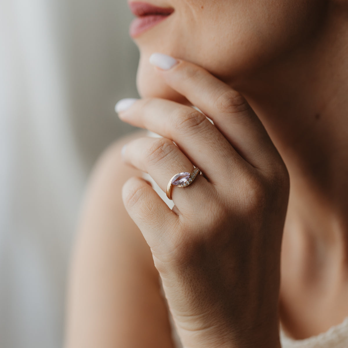 Primo piano di una mano vicino al viso che indossa l'anello Velvet Rose in oro giallo 14K con uno zaffiro rosa taglio marquise e piccoli diamanti di contorno.