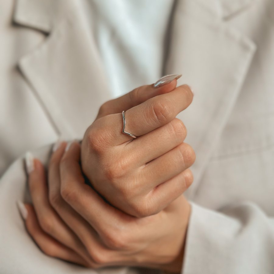 Primo piano di una mano che indossa un anello minimalista a forma di V in argento.