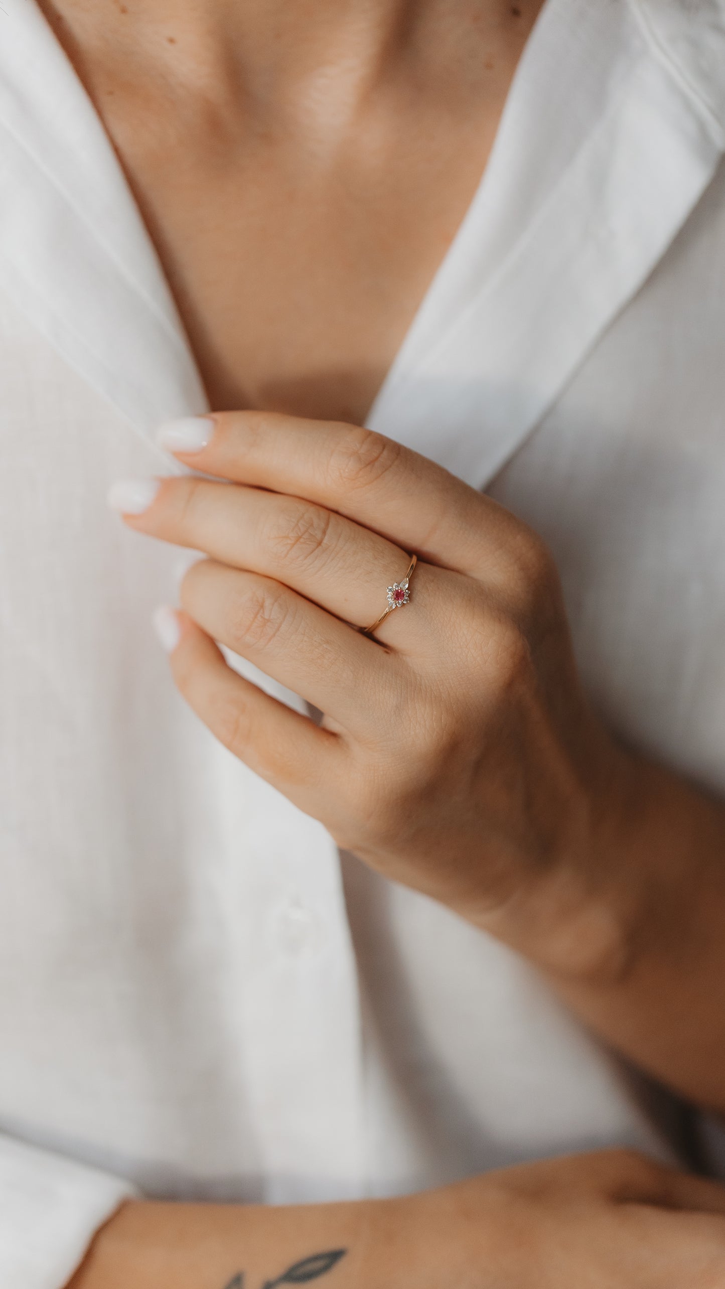 Primo piano di una mano che indossa un delicato anello in oro giallo con una tormalina rosa centrale e un contorno di zaffiri bianchi.
