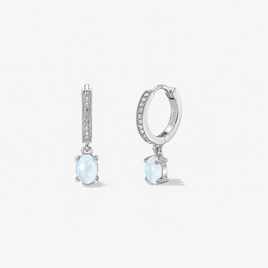 Orecchini huggie in argento 925 con cerchi pavé e pendenti con pietra di luna ovale, azzurro lattiginoso; coppia fotografata su fondo bianco, vista frontale e laterale.