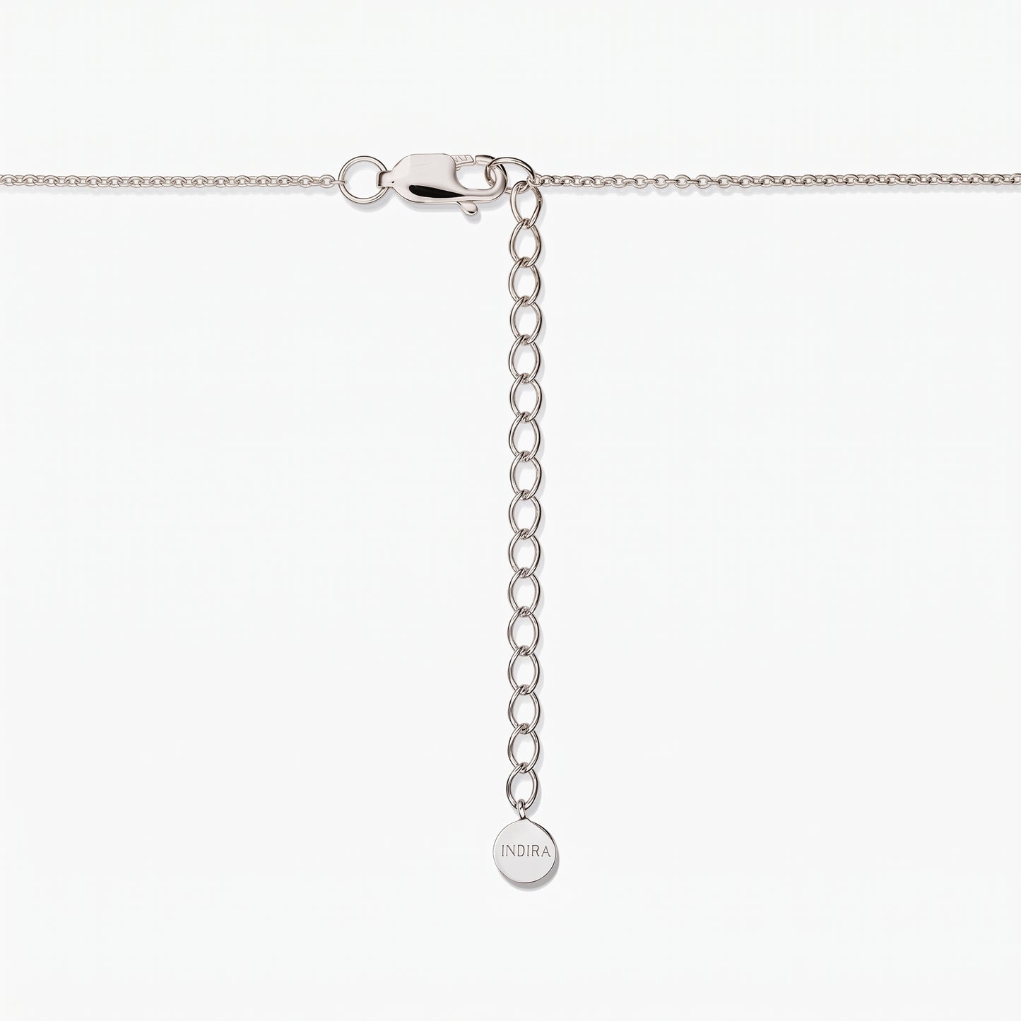 Primo piano della chiusura di una collana in argento sterling con catenina di prolunga regolabile e una piccola targhetta rotonda incisa “INDIRA”, su sfondo bianco.