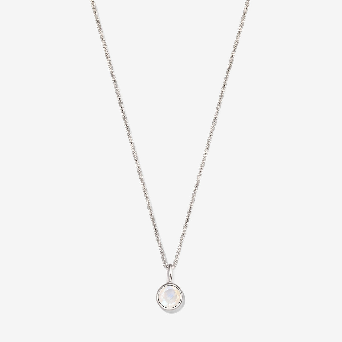 Collana in argento sterling con un piccolo pendente rotondo in pietra di luna incastonata a castone su una catena sottile, fotografata su sfondo bianco.