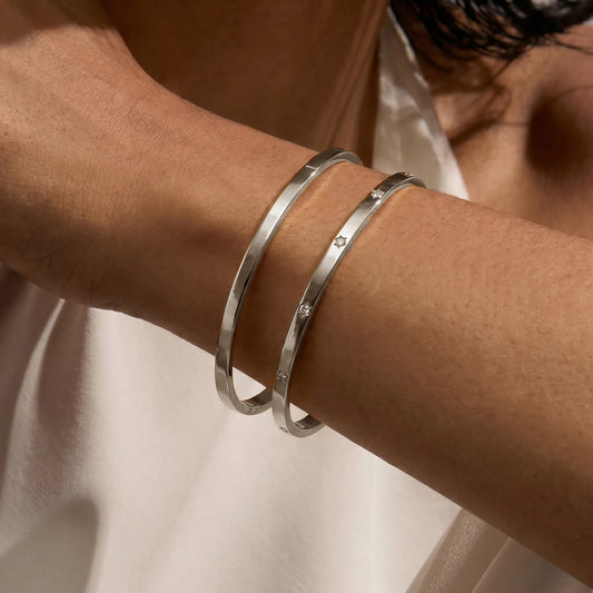 Primo piano di un polso ornato con due braccialetti minimalisti in argento. Uno è semplice, l'altro presenta piccole pietre di zirconia.