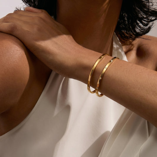 Primo piano di un braccio con indosso due bracciali a cerchio in oro su sfondo bianco.