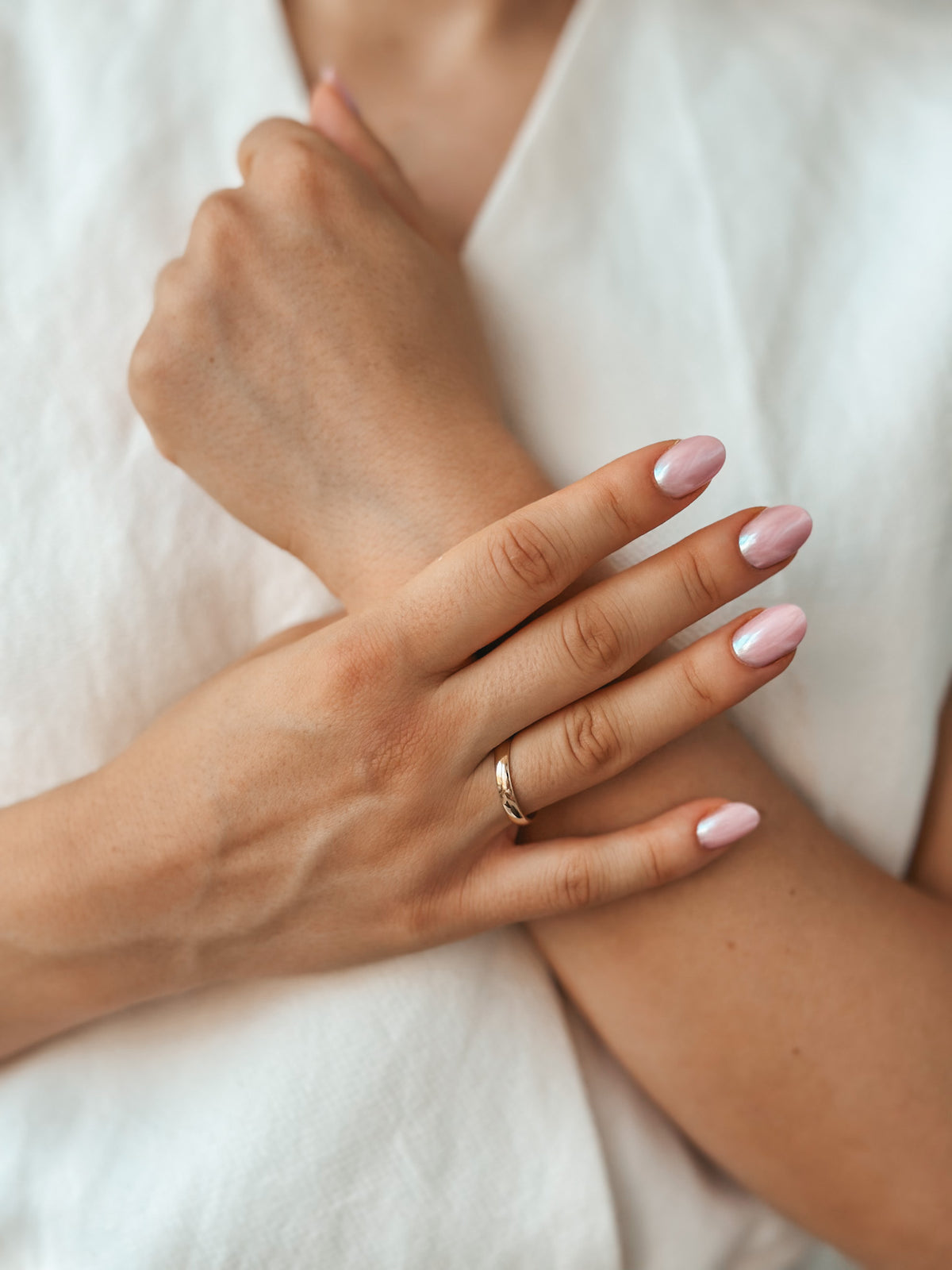 Primo piano di una mano che indossa una fede nuziale ampia e arrotondata in oro con nail art rosa e argento.