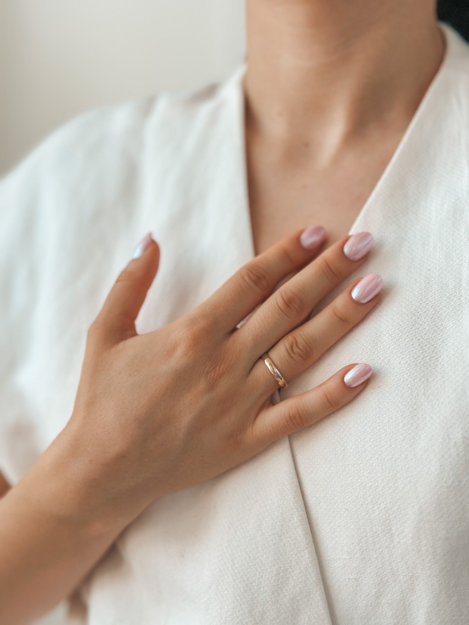Close-up of a hand with a gold wedding band and manicured nails against a white fabric.