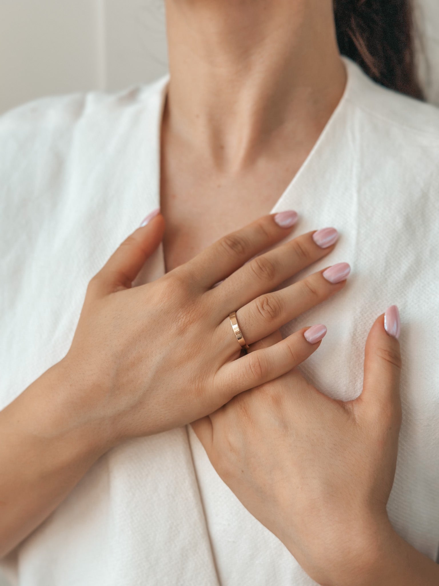 Close-up image of hands with a simple gold wedding band on the ring finger, against a white cloth background.
