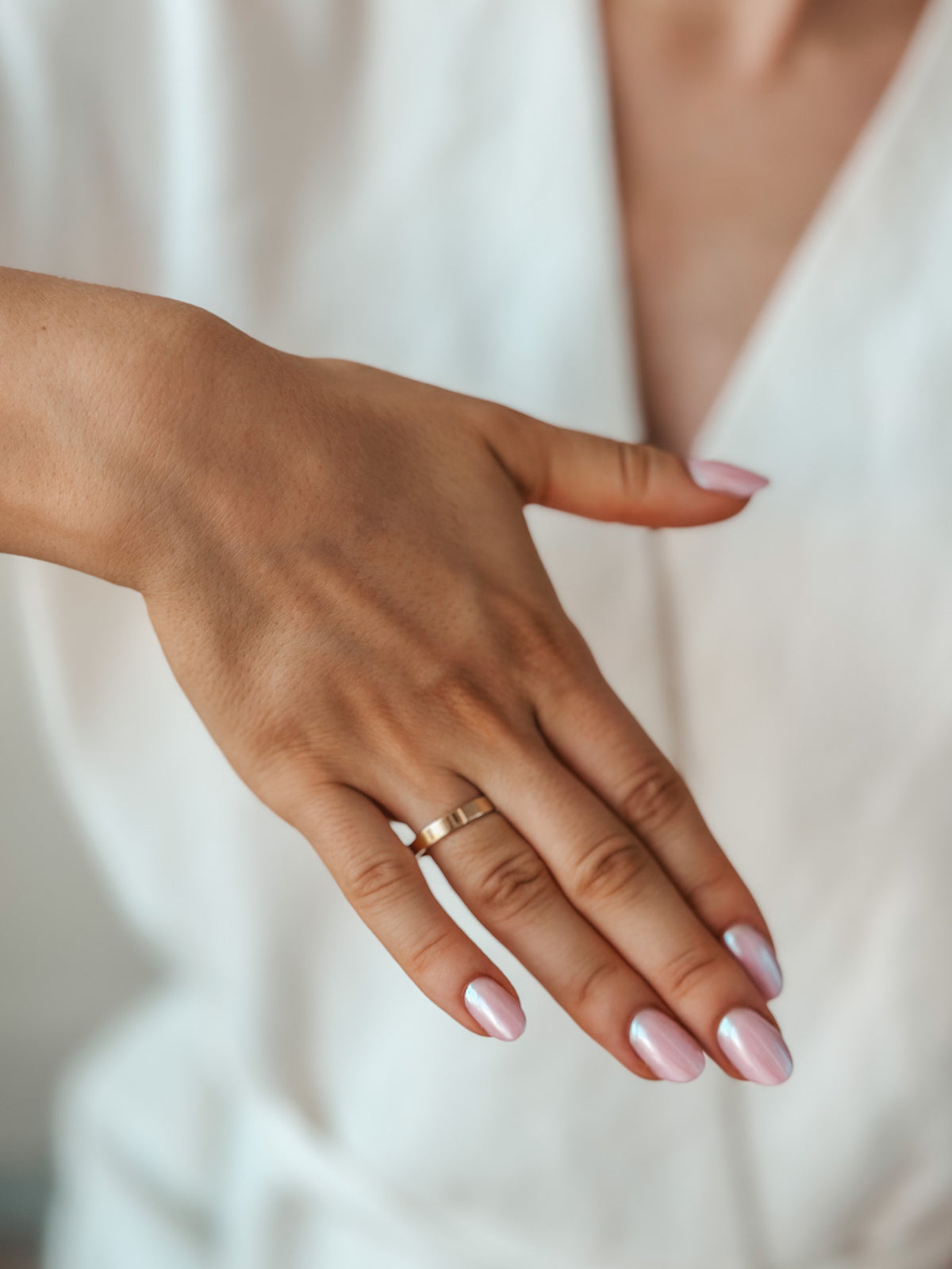 Una mano che mostra una semplice fede in oro, con unghie smaltate di rosa.