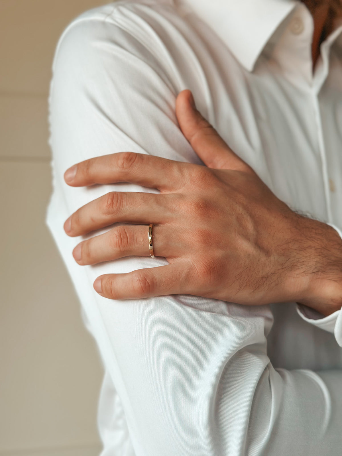 Primo piano di una mano con un anello nuziale in oro sul braccio di una camicia bianca.