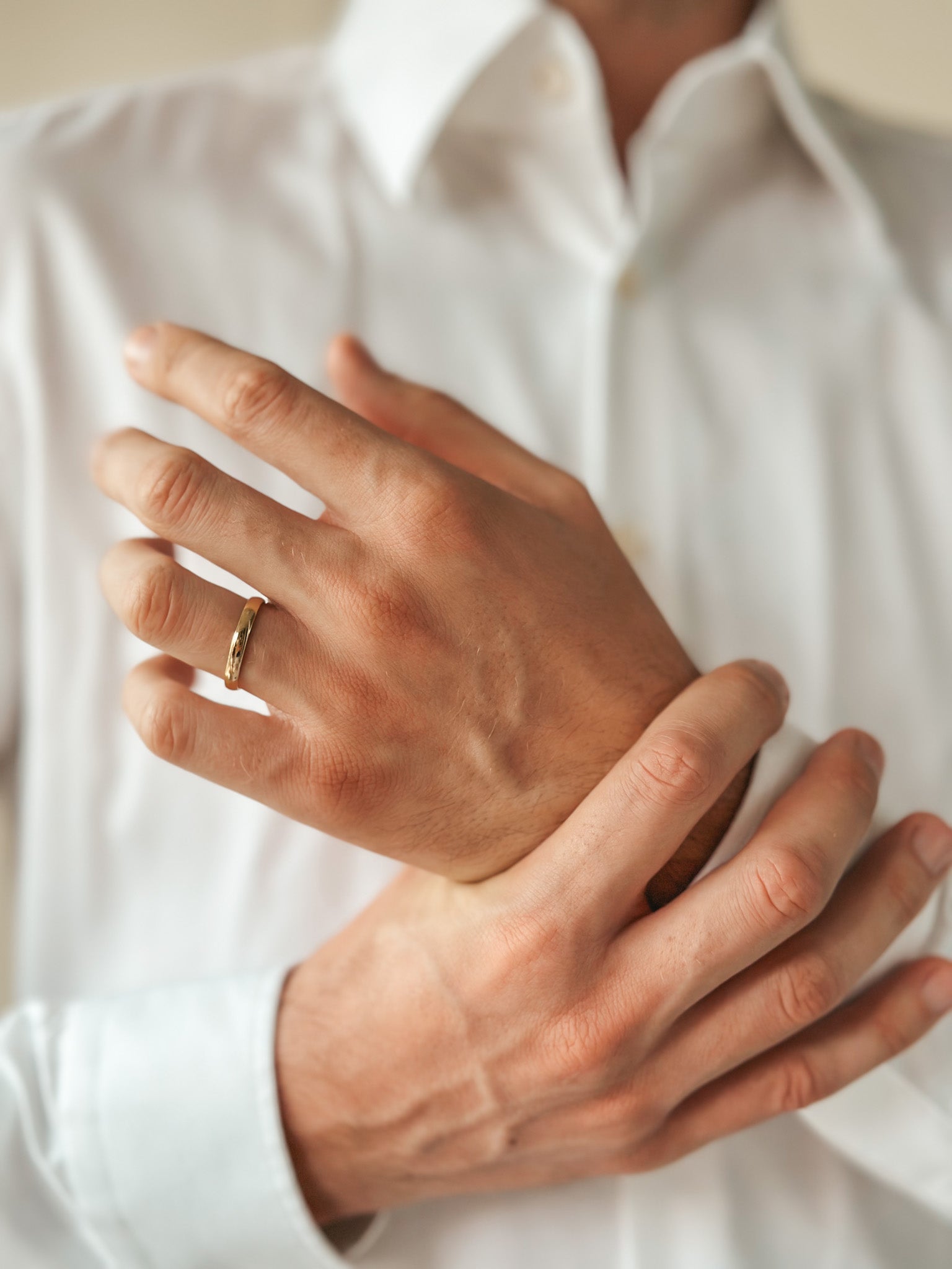 Primo piano di mani che mostrano una fede nuziale in oro sull'anulare, indossando una camicia bianca.