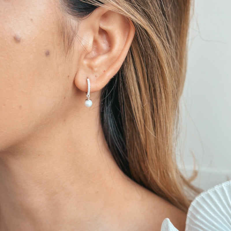 Primo piano dell'orecchio di una donna che indossa orecchini in argento dal design con perla e zirconi.