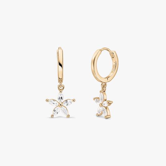 Orecchini huggie a cerchio in argento sterling placcato oro con ciondoli a forma di fiore in topazio bianco su sfondo bianco.