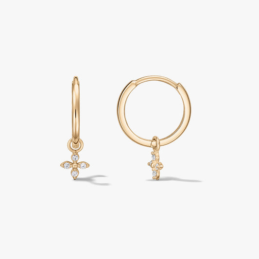 Coppia di orecchini a cerchio in oro giallo 14K con piccoli ciondoli a fiore a quattro petali con pavé di zirconi, su sfondo bianco.