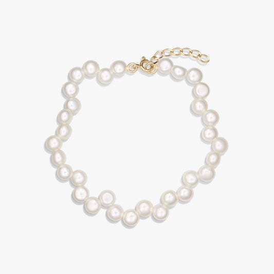 Bracciale in argento 925 placcato oro con perle bianche naturali e catenina di prolunga regolabile, fotografato su sfondo bianco.