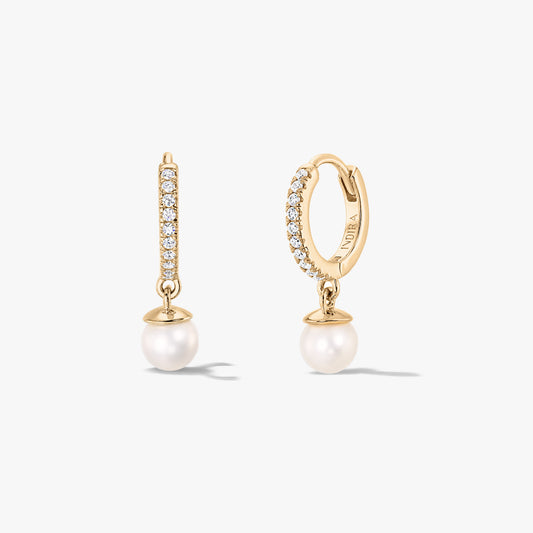 Coppia di orecchini a cerchio huggie in argento con finitura dorata, con pavé di zirconi e pendenti con perle naturali bianche di Indira, mostrati frontalmente e lateralmente su sfondo bianco.