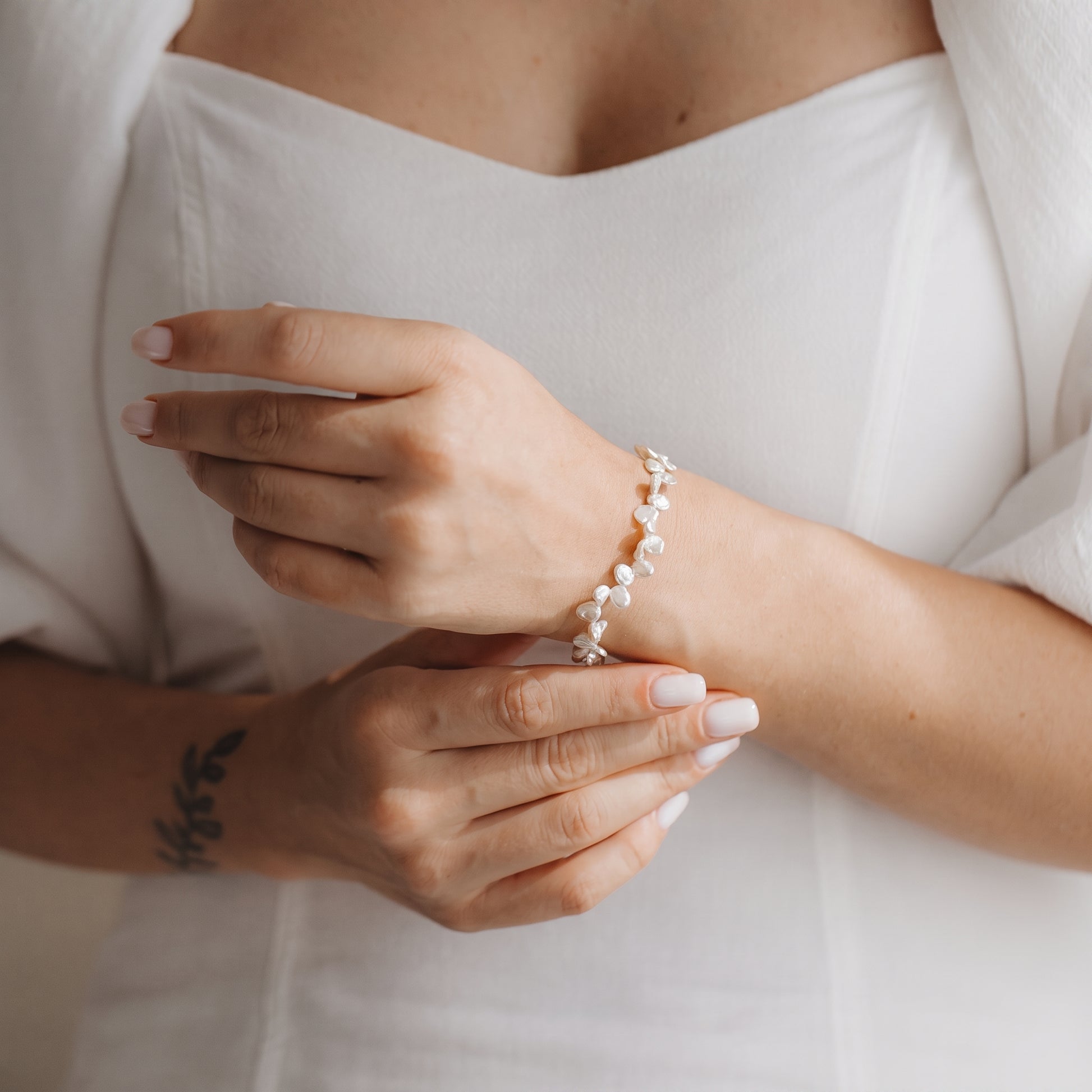 Primo piano delle mani che indossano un bracciale in argento sterling placcato oro con perle keshi bianche, sullo sfondo di un abito bianco.
