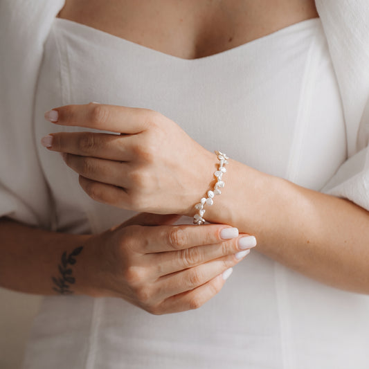 Primo piano delle mani che indossano un bracciale in argento sterling placcato oro con perle keshi bianche, sullo sfondo di un abito bianco.