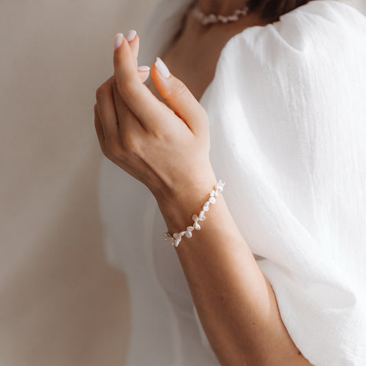 Primo piano di un polso con un delicato bracciale di perle Keshi in argento sterling, fotografato in luce naturale soffusa su una camicetta bianca.