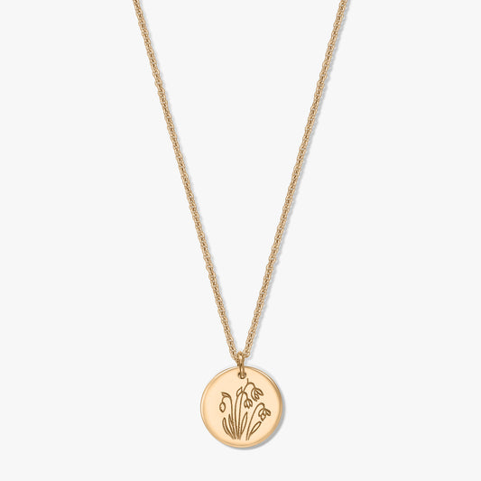 Collana in argento sterling placcato in oro con ciondolo a disco rotondo inciso con il fiore di nascita di gennaio, il bucaneve, su sfondo bianco.