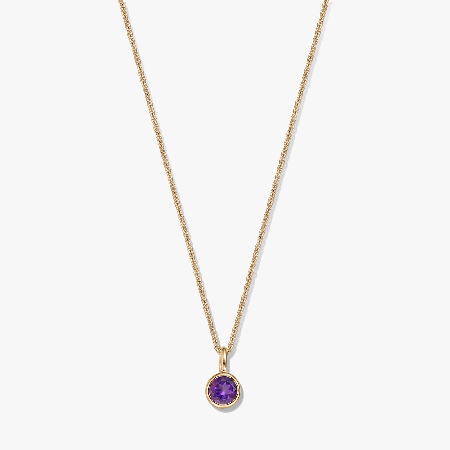 Collana in argento sterling placcato oro con un piccolo pendente rotondo con ametista come pietra di nascita su sfondo bianco.