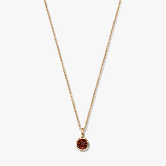 Elegante collana in argento sterling placcato oro con ciondolo in granato rotondo montato a castone su catena delicata, isolata su sfondo bianco.