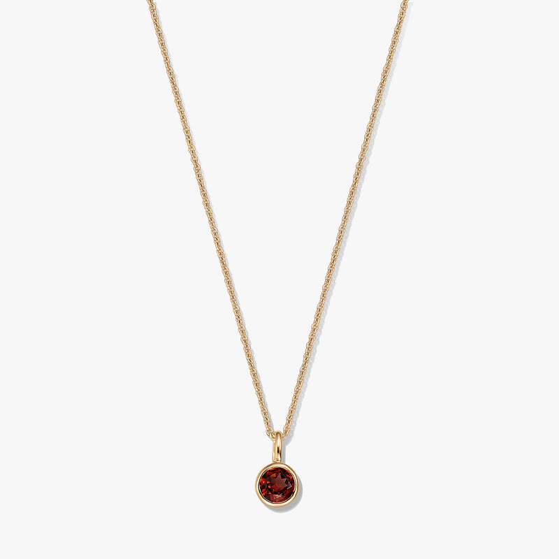 Elegante collana in argento sterling placcato oro con ciondolo in granato rotondo montato a castone su catena delicata, isolata su sfondo bianco.
