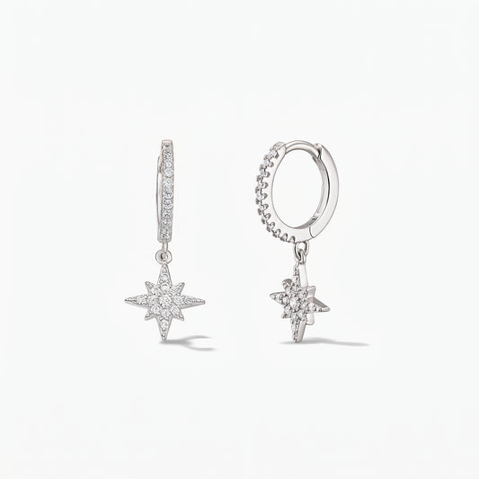 Coppia di orecchini a cerchio huggie in argento sterling 925 con ciondoli a forma di Stella Polare impreziositi da pavé di zirconi bianchi su sfondo bianco.