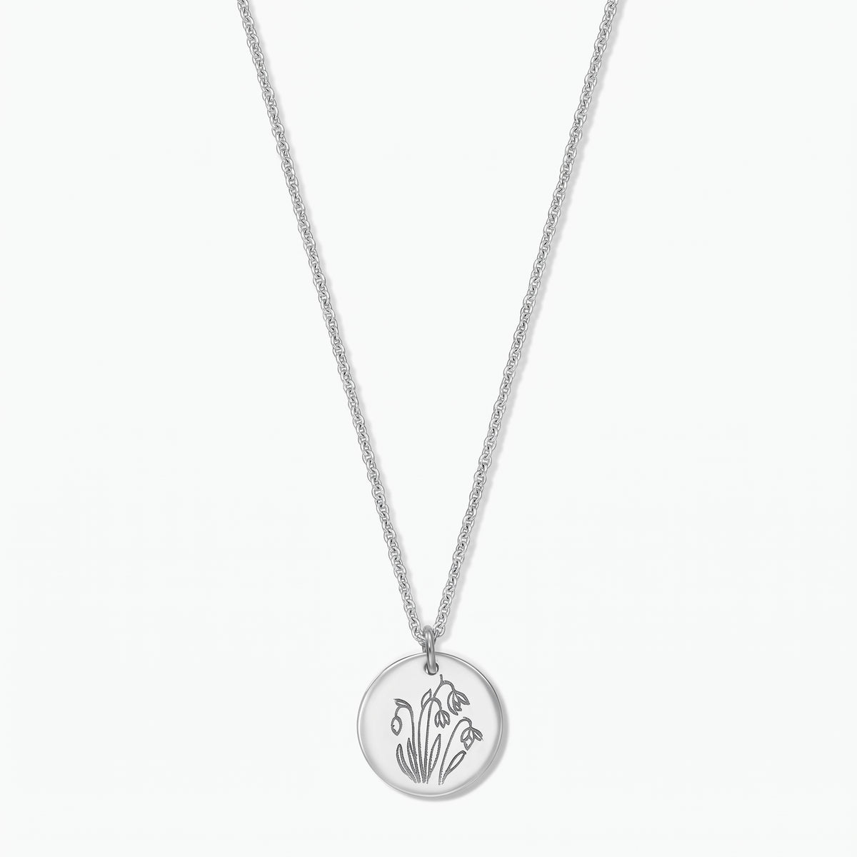 Collana in argento sterling con fiore di nascita, ciondolo a disco rotondo inciso con i bucaneve di gennaio su una catena fine, isolata su sfondo bianco.