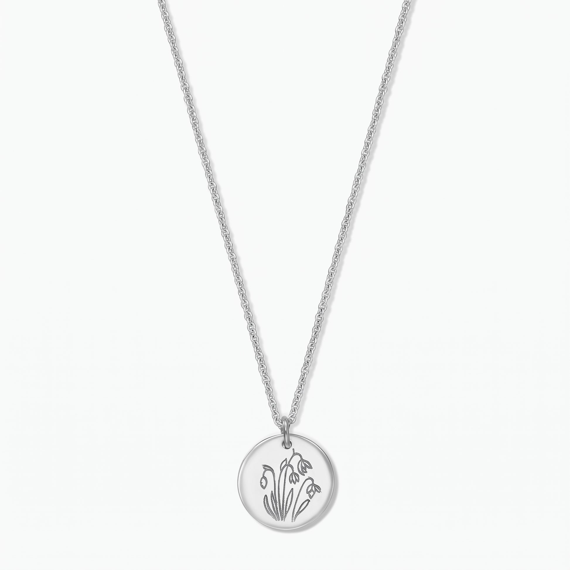 Collana in argento sterling con fiore di nascita, ciondolo a disco rotondo inciso con i bucaneve di gennaio su una catena fine, isolata su sfondo bianco.