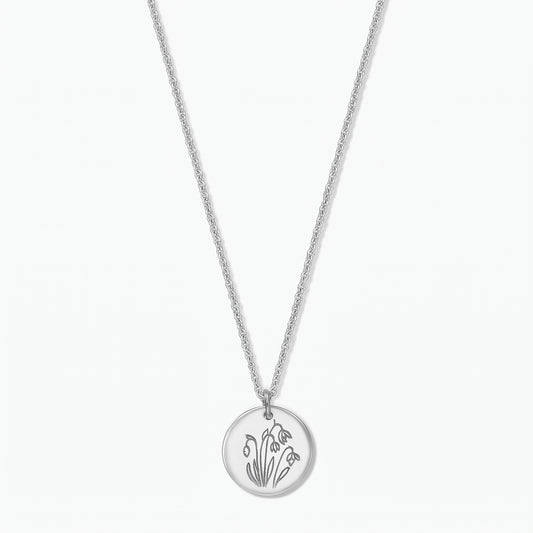 Collana in argento sterling con fiore di nascita, ciondolo a disco rotondo inciso con i bucaneve di gennaio su una catena fine, isolata su sfondo bianco.