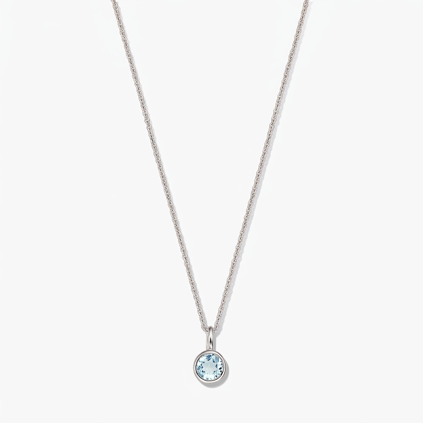 Elegante collana in argento sterling con pietra di nascita e piccolo ciondolo rotondo in topazio blu con montatura a castone, su sfondo bianco.