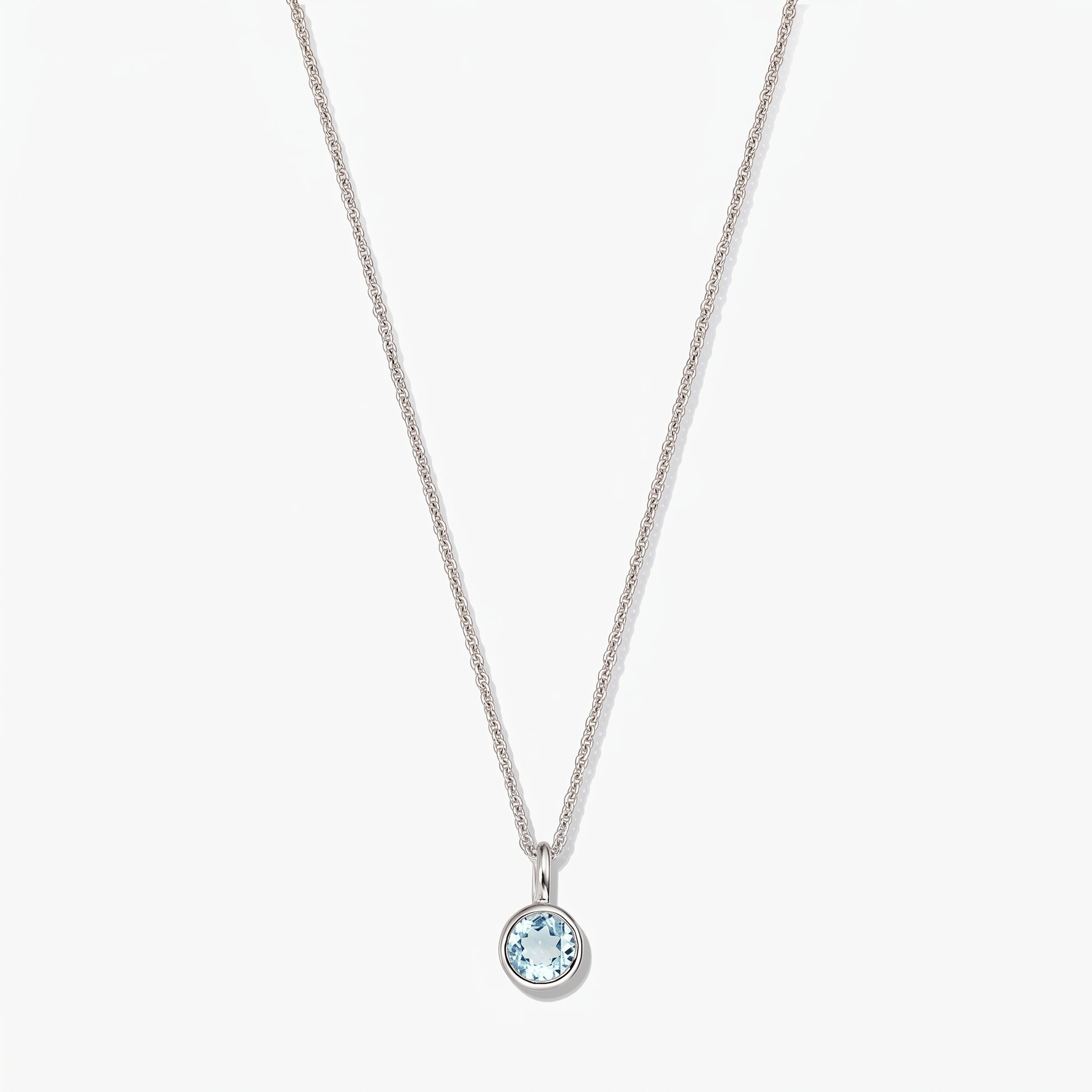 Elegante collana in argento sterling con pietra di nascita e piccolo ciondolo rotondo in topazio blu con montatura a castone, su sfondo bianco.
