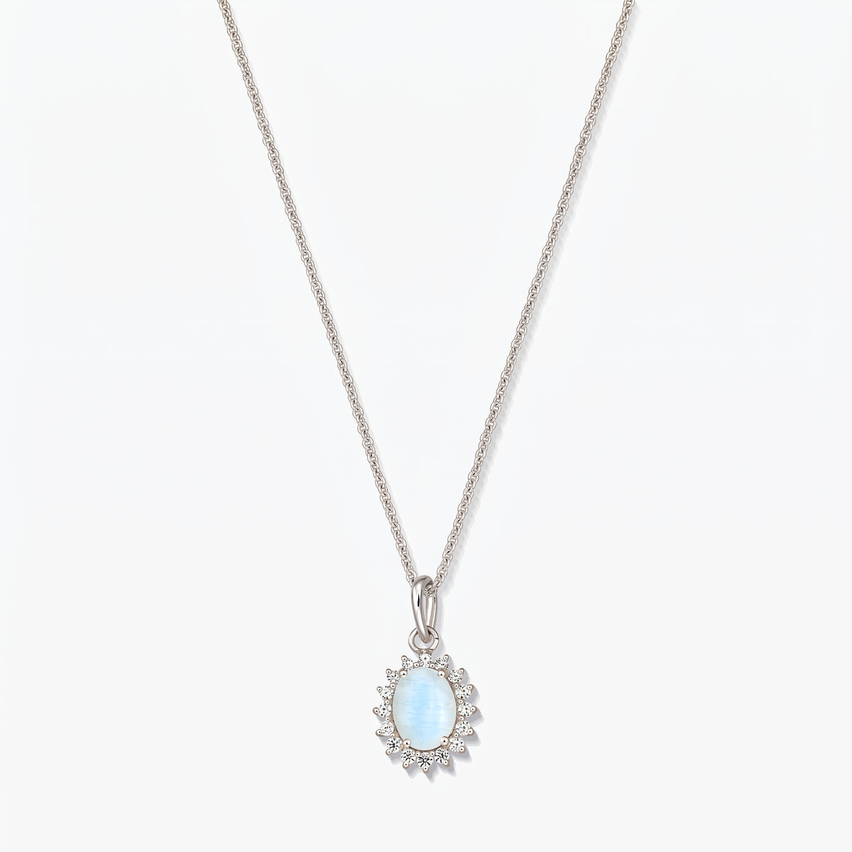 Collana in argento sterling con pendente ovale in pietra di luna di colore azzurro chiaro, contornato da piccole pietre trasparenti su una catena sottile, fotografata su sfondo bianco.
