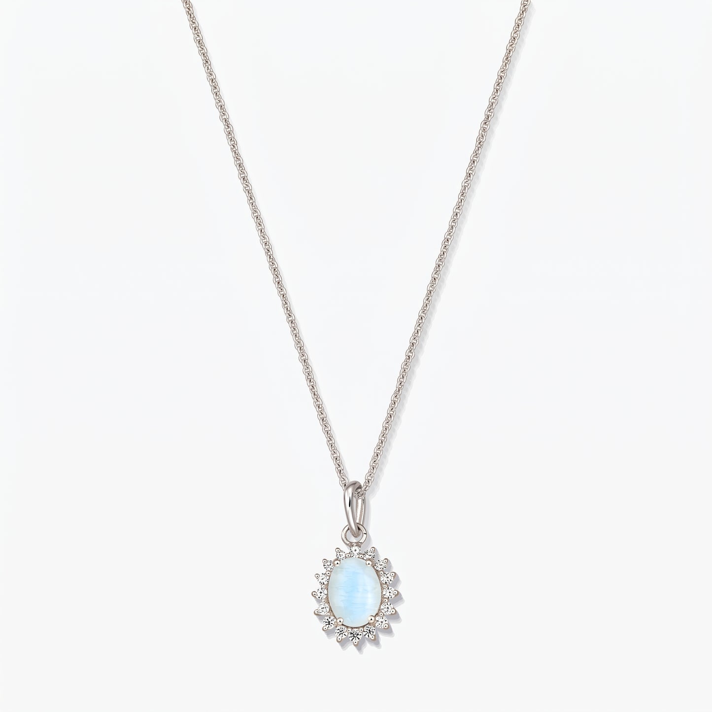 Collana in argento sterling con pendente ovale in pietra di luna di colore azzurro chiaro, contornato da piccole pietre trasparenti su una catena sottile, fotografata su sfondo bianco.