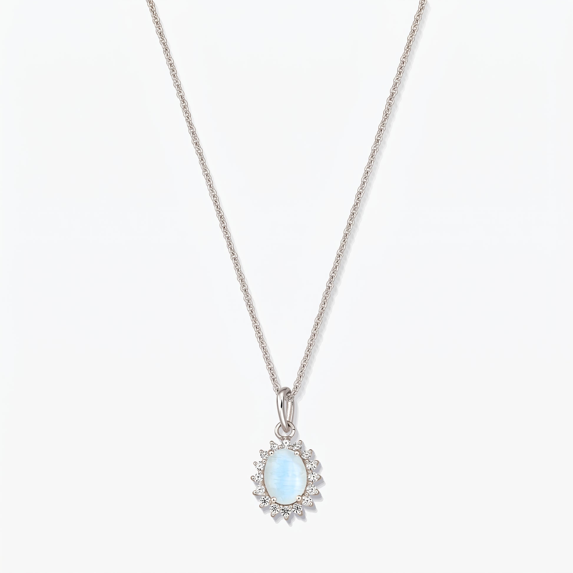 Collana in argento sterling con pendente ovale in pietra di luna di colore azzurro chiaro, contornato da piccole pietre trasparenti su una catena sottile, fotografata su sfondo bianco.
