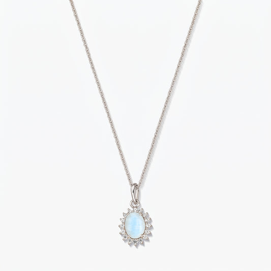 Collana in argento sterling con pendente ovale in pietra di luna di colore azzurro chiaro, contornato da piccole pietre trasparenti su una catena sottile, fotografata su sfondo bianco.