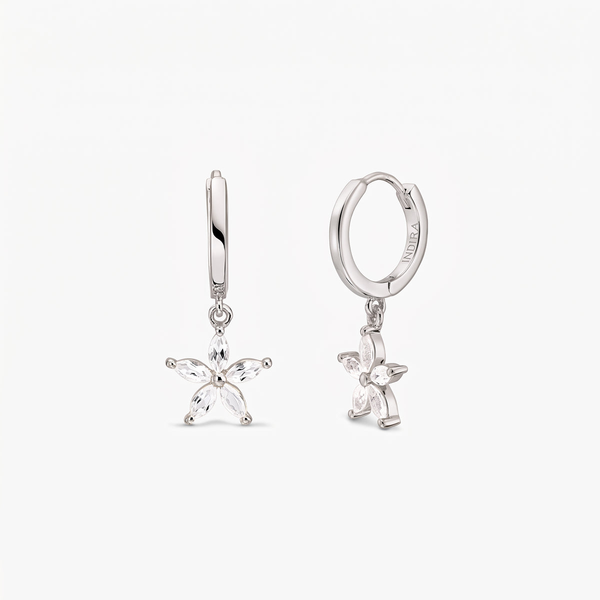 Coppia di orecchini a cerchio huggie in argento sterling con ciondoli pendenti a fiore a cinque petali incastonati con topazi bianchi, su sfondo bianco.