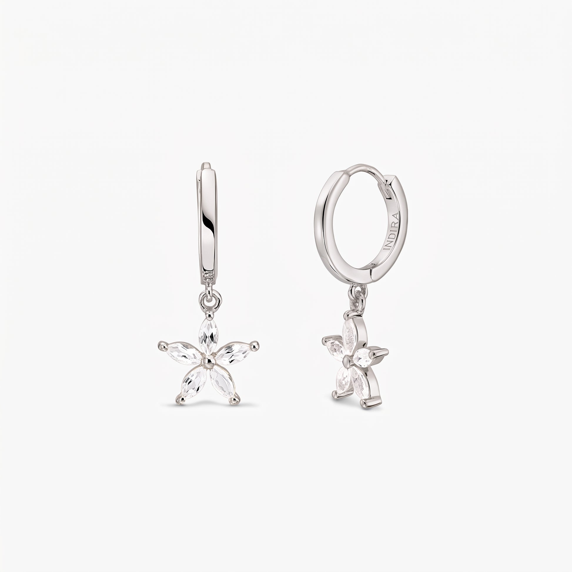 Coppia di orecchini a cerchio huggie in argento sterling con ciondoli pendenti a fiore a cinque petali incastonati con topazi bianchi, su sfondo bianco.