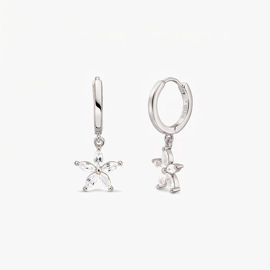 Coppia di orecchini a cerchio huggie in argento sterling con ciondoli pendenti a fiore a cinque petali incastonati con topazi bianchi, su sfondo bianco.
