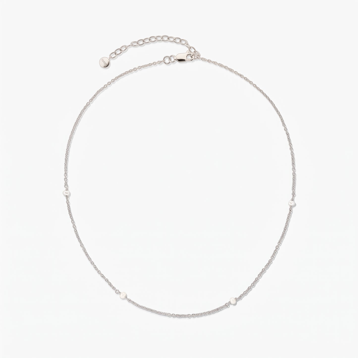 Collana a catena in argento, elegante e delicata, con piccole perle bianche a intervalli; disposta a cerchio su sfondo bianco, con prolunga regolabile e chiusura a moschettone.