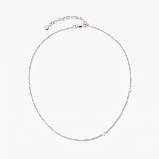 Collana a catena in argento, elegante e delicata, con piccole perle bianche a intervalli; disposta a cerchio su sfondo bianco, con prolunga regolabile e chiusura a moschettone.