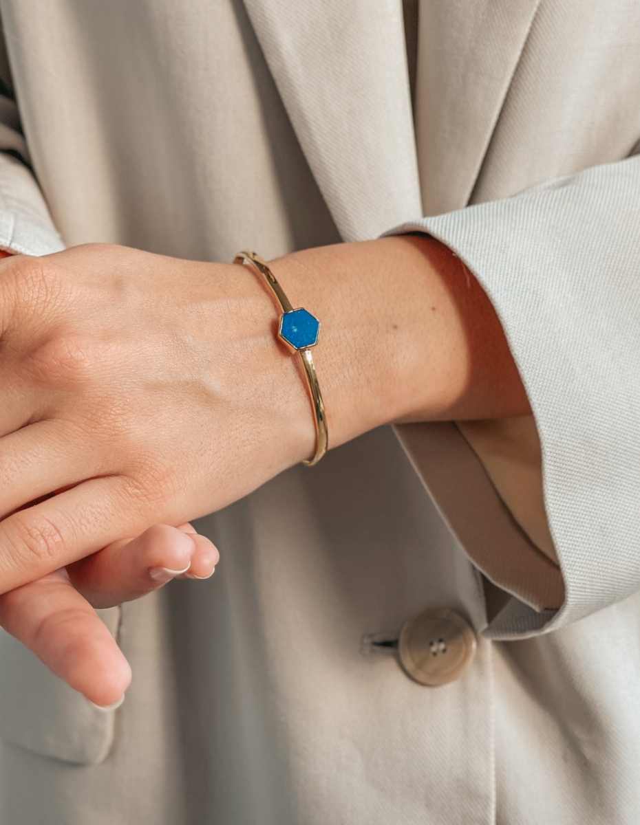 Una mano che indossa un braccialetto d'argento con una pietra di lapislazzuli blu, su uno sfondo di abbigliamento beige chiaro.
