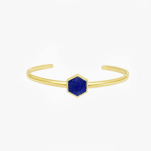 Bracciale rigido in argento color oro con pietra centrale esagonale in lapislazzuli blu su sfondo bianco.